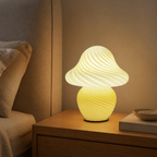 Yellow swirled glass mushroom table lamp glowing on an oak bedside table