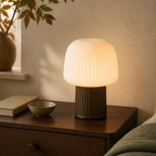 Ribbed ivory table lamp lit on a walnut bedside table