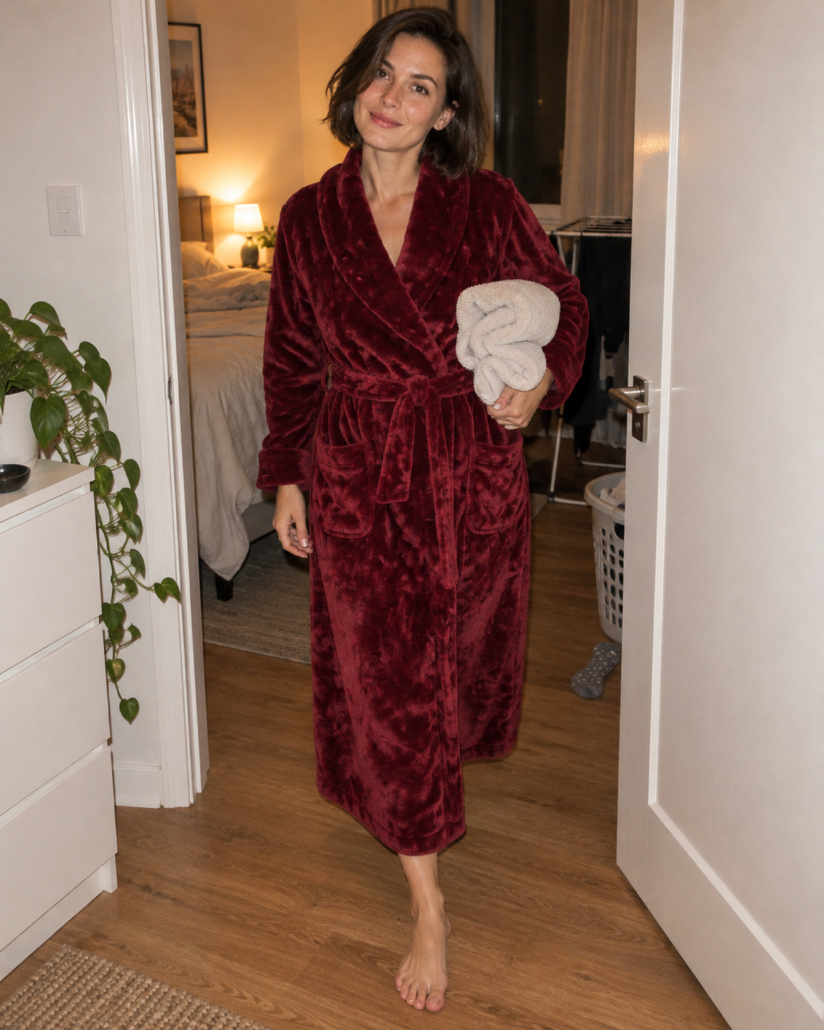 Woman carrying folded towels in a long burgundy fleece dressing gown