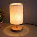 Warm light shining through the beige shade of the round wooden table lamp