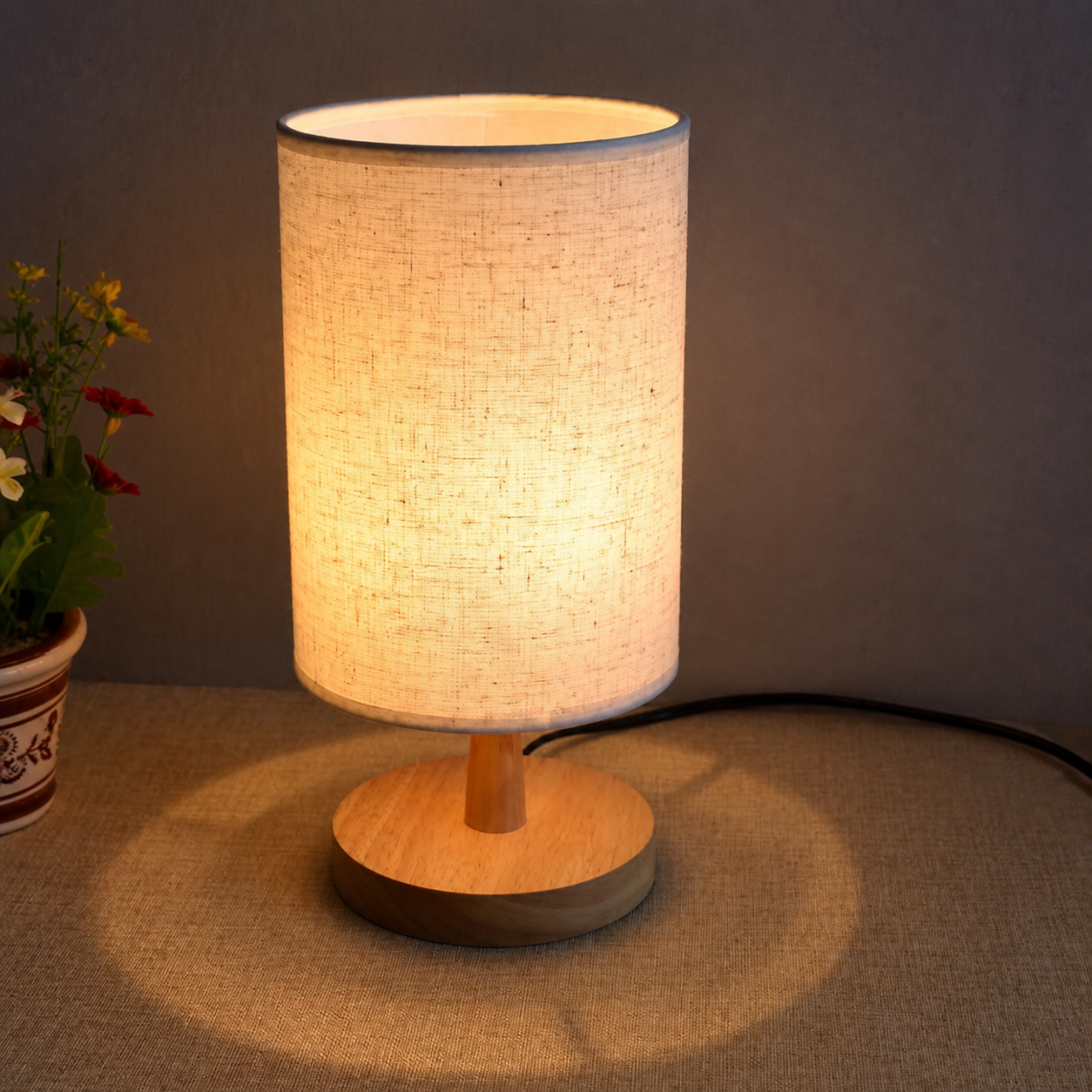 Warm light shining through the beige shade of the round wooden table lamp